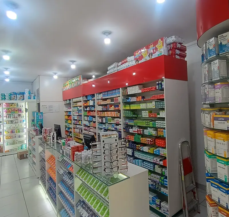 Interior de farmácia com balcões de vidro e parede de medicamentos